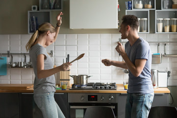 Funny young couple dancing to music together enjoying cooking in the kitchen, man and woman in love having fun preparing breakfast food feeling happy and carefree on weekend lifestyle at home - Powered by Adobe