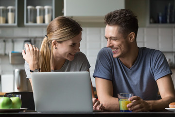 Young happy positive family couple talking laughing during breakfast with laptop, funny cheerful...