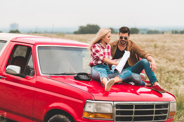 travelling young couple sitting on car engine hood and navigating with map