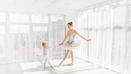 Fototapeta na wymiar Young gorgeous ballerina with her little daughter dancing in studio