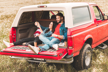 beautiful young couple taking selfie with smartphone while relaxing in car trunk