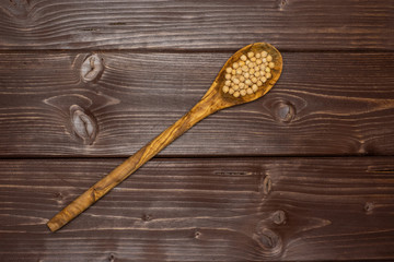 Lot of whole raw chickpeas kabuli variety with olivewood spoon flatlay on brown wood