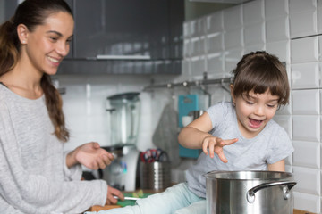 Curious funny kid girl playing with pot with mom in the kitchen, excited active child helping...