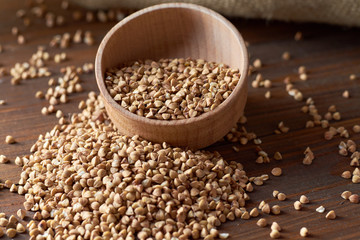 Buckwheat is rash out of a wooden container on a dark wooden table