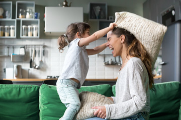 Mommy and kid daughter having pillow fight together, young babysitter nanny playing funny game with kid girl at home, happy mother and child enjoy spending time together, family leisure fun activity - Powered by Adobe