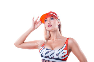 A blonde girl in a red cap with a transparent visor and a multicolour swimsuit holds on to the cap of a cap on a white background.