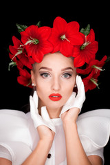 Naklejka premium Portrait of a girl in white with a wreath of red flowers on her head, holding her hands in white gloves next to her face on a black background
