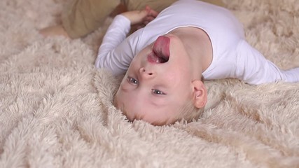 Funny little boy of 4 years is lying on the bed and shows tongue. Portrait of little boy with blond hair in the bedroom, he's having fun and showing tongue.