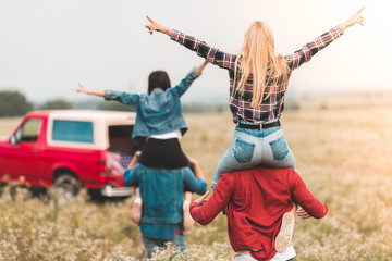 rear view of young women riding on boyfriends shoulders in field