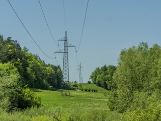 High voltage power electricity lines with high pilars going through green land.