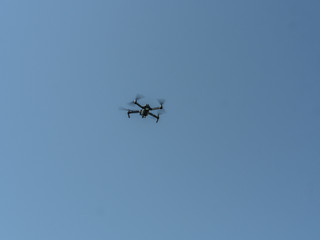 Foldable filming drone in flight with blue sky in background.