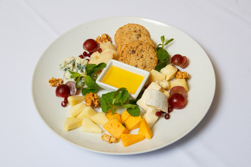 Dessert from a cookie, cheeses, nuts, plum, mint, on a white dish with a sauce. General view. White...