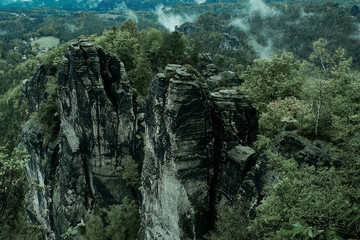 Rocky mountain view during autumn season. Foggy sunrise at Bastei, Saxon Switzerland, Germany. Misty landscape with fir forest in hipster vintage retro style