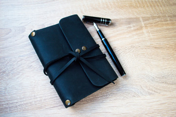 Men's business accessories - a black leather notepad, fountain pen on the office desk. Business and education.
