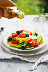 Hand pours olive oil in a plate with fresh summer salad in the background natural mode.