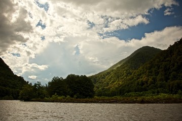 Fototapeta na wymiar Summer landscape. Sky with clouds over mountain river. Mist over green forest.