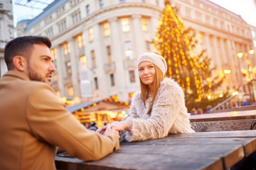 A beautiful young couple sitting and holding hands in a christmas market.
