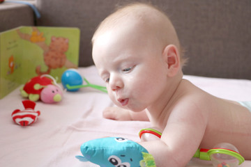 Little cute white baby looking at toys laying on stomach