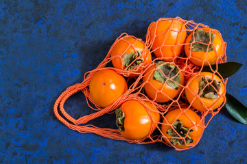 Ripe persimmon in orange string bag