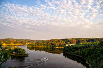 Obraz premium Colourful sunset over a lake. Summer scene of wide river landscape with setting sun. Small boat sails in river.