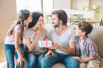 Amazed woman looks at present that man holds. She is surprised and happy. Kids look at parents.