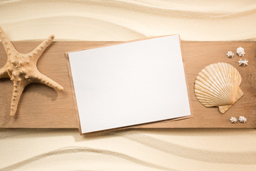 Fototapeta na wymiar flat lay with blank paper, sea star and seashells on wooden plank on sand