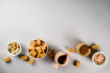 Salted caramel sauce with fudge candy, fleur de sel, brown cane sugar, grey background copy space top view