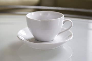 An empty white cup and a saucer stand on a coffee table.