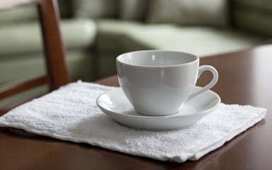 An empty white cup and a saucer stand on a wooden table.