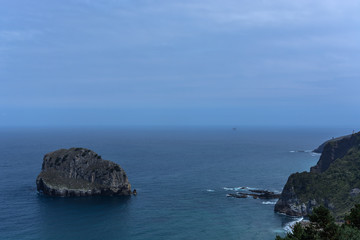 Fototapeta na wymiar Composition of a little rocky island apart of a rocky coast & the atlantic ocean's horizon at the Basque Country, Spain
