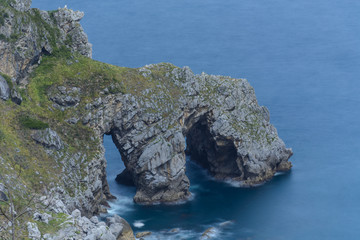 Fototapeta na wymiar A natural made rocky arch above the atlantic ocean wit some foliage at the Basque Country, Spain