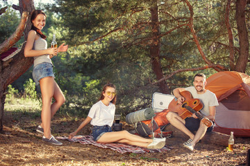 Party, camping of men and women group at forest. They relaxing, singing a song against green grass. The vacation, summer, adventure, lifestyle, picnic concept