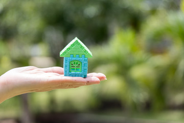 Woman hand hold home block model with blur green background (Concept for dream home, family fulfillment)