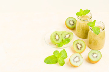 Kiwi smoothie decorated with fresh green mint leaves and raw ripe cut fruit on yellow pastel background.