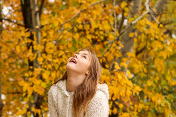 Beautiful happy young girl looking up with smile on her face in autumn park with yellow leaves on background. Happiness, dreams, hope.