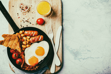 English Breakfast in a skillet. Eggs in the Heart shape. Valentine's Day. Festive Food on the Blue Background.Sausages, Bacon, Beans,Orange juice and Coffee.Copy space for Text Toned image
