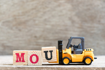 Toy forklift hold letter block u in word mou (abbreviation of memorandum of understanding) on wood background