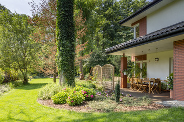 Green grass and trees next to garden furniture on terrace of house with roof