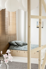 Flowers and blinds in white bedroom interior with patterned cushions on wooden bed. Real photo