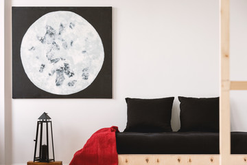 Red blanket and black pillows on wooden bed in bedroom interior with moon poster and lantern. Real...