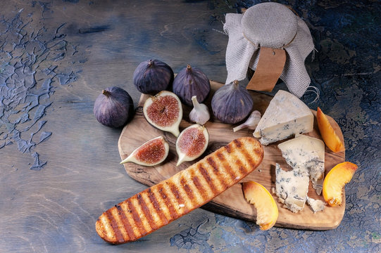 Ripe figs, noble cheese with mold, peach slices and baguette on a cutting board.