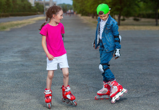 In the summer in the park, a boy and a girl roll on roller skates.