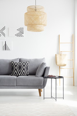 Real photo of a boho, black and white pillow on a gray couch standing next to a black, metal coffee table in white living room interior