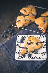Homemade Blueberry Scones on a White Bon Appetite Dish; More Scones in Background on Wire Rack; Deep Blue Napkin; Black Background