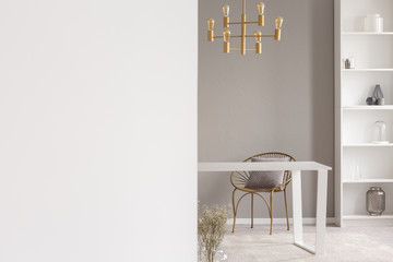 Copy space on white wall in living room interior with chair at table under gold chandelier. Real photo with a place for your poster