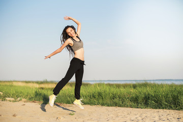 A cheerful sports girl with dreadlocks, in yellow sneakers, black pants and a top, jumps on the...