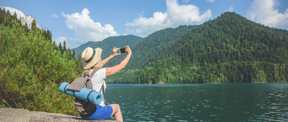 Beautiful Girl Traveler takes pictures of a large blue mountain lake in the background of the mountains