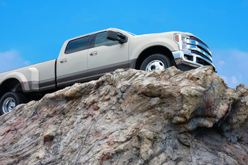 Big rugged pickup truck driving on the edge of a rocky cliff ledge with a bright blue sky in the...