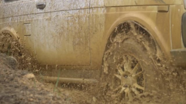 Beautiful car in rough terrain. A powerful SUV is towed in a deep puddle. Extreme driving conditions in the countryside. Flying from under the wheels of spray and dirt.