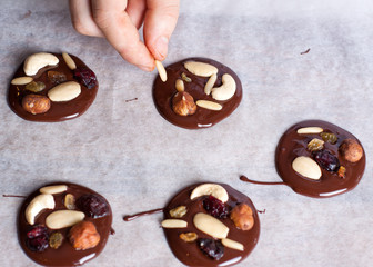 Homemade chocolate snacks with nuts and berries preparation, Man adding almond to chocolate circles
